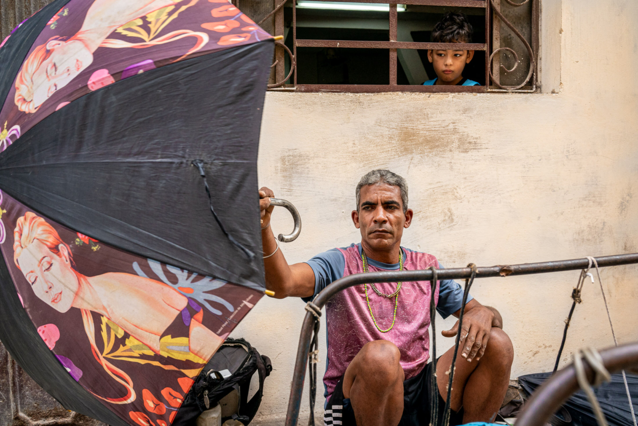Cuba Street Photography Roadtrp | 14 Day Guide with Mark Seymour 1 “Cuban man holding a brightly patterned umbrella while a young boy observes him from a window above.”