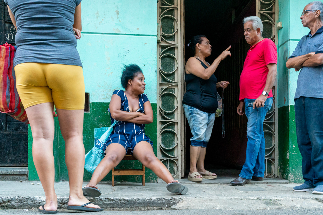 Cuba Street Photography Roadtrp | 14 Day Guide with Mark Seymour 13 “Cuban neighbours gathered outside a turquoise building, talking animatedly while a woman sits casually on a small chair.”