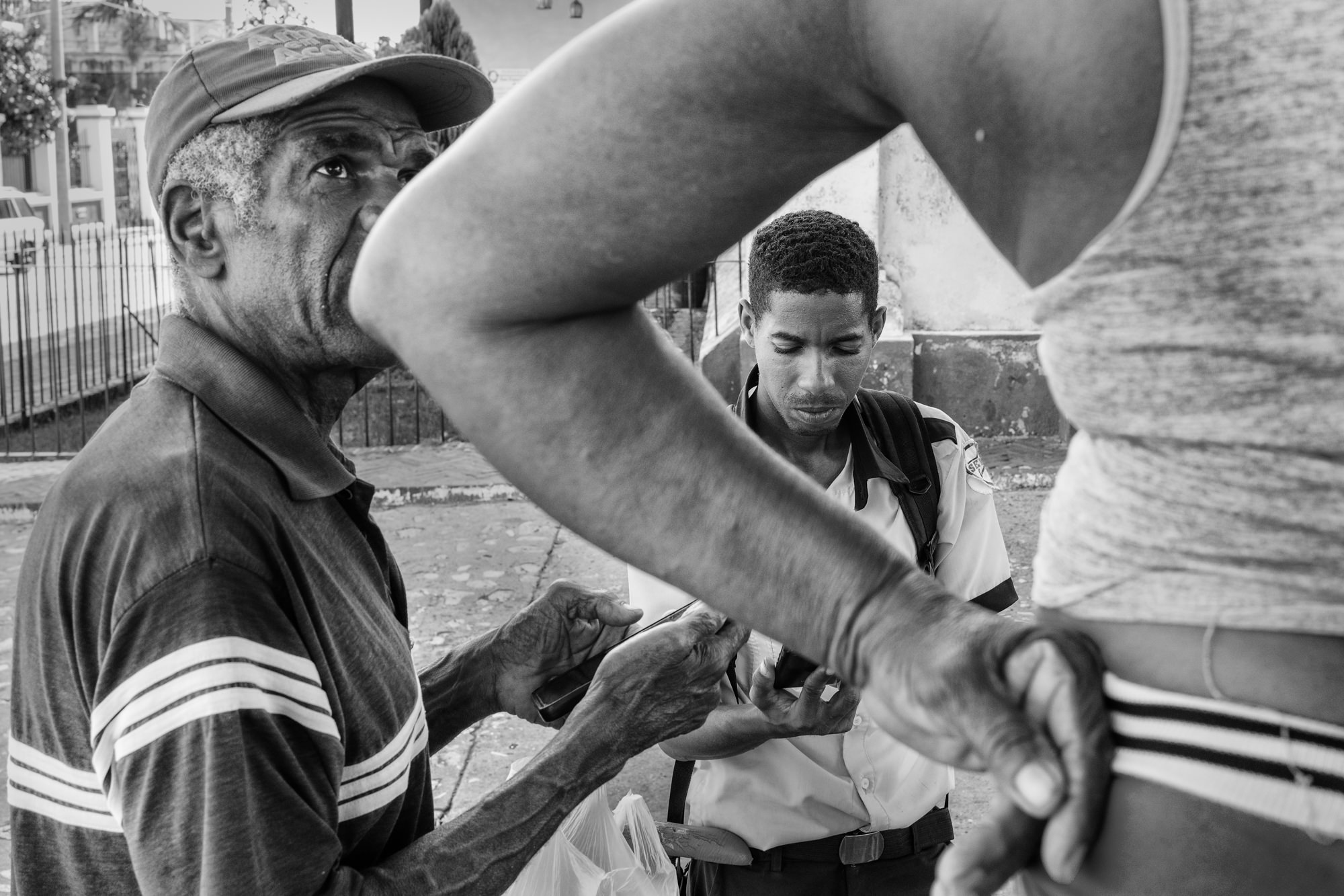 Cuba Street Photography Roadtrp | 14 Day Guide with Mark Seymour 29 “Black-and-white scene of two Cuban men examining a phone while another person’s arm crosses the foreground.”