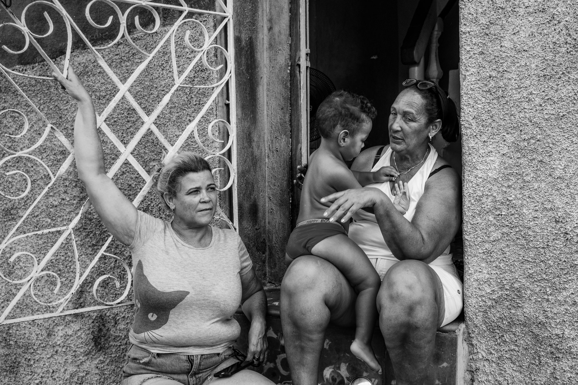 Cuba Street Photography Roadtrp | 14 Day Guide with Mark Seymour 26 “Two Cuban women sitting in a doorway talking while a young child rests on one woman’s lap, captured in black and white.”