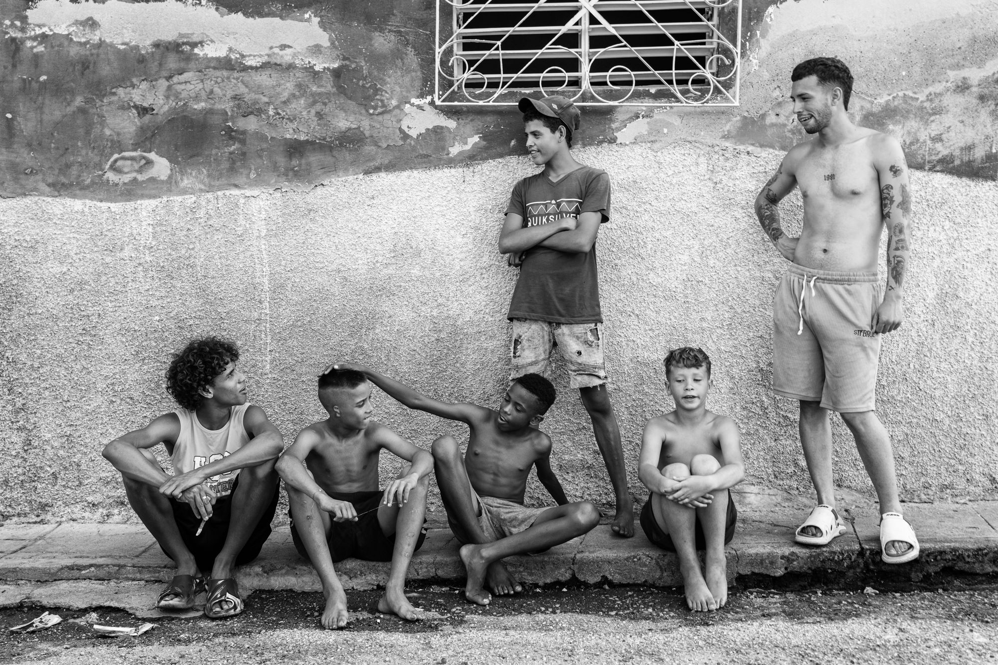 Cuba Street Photography Roadtrp | 14 Day Guide with Mark Seymour 24 “Cuban boys and young men sitting and standing along a textured wall in a relaxed black-and-white street scene.”