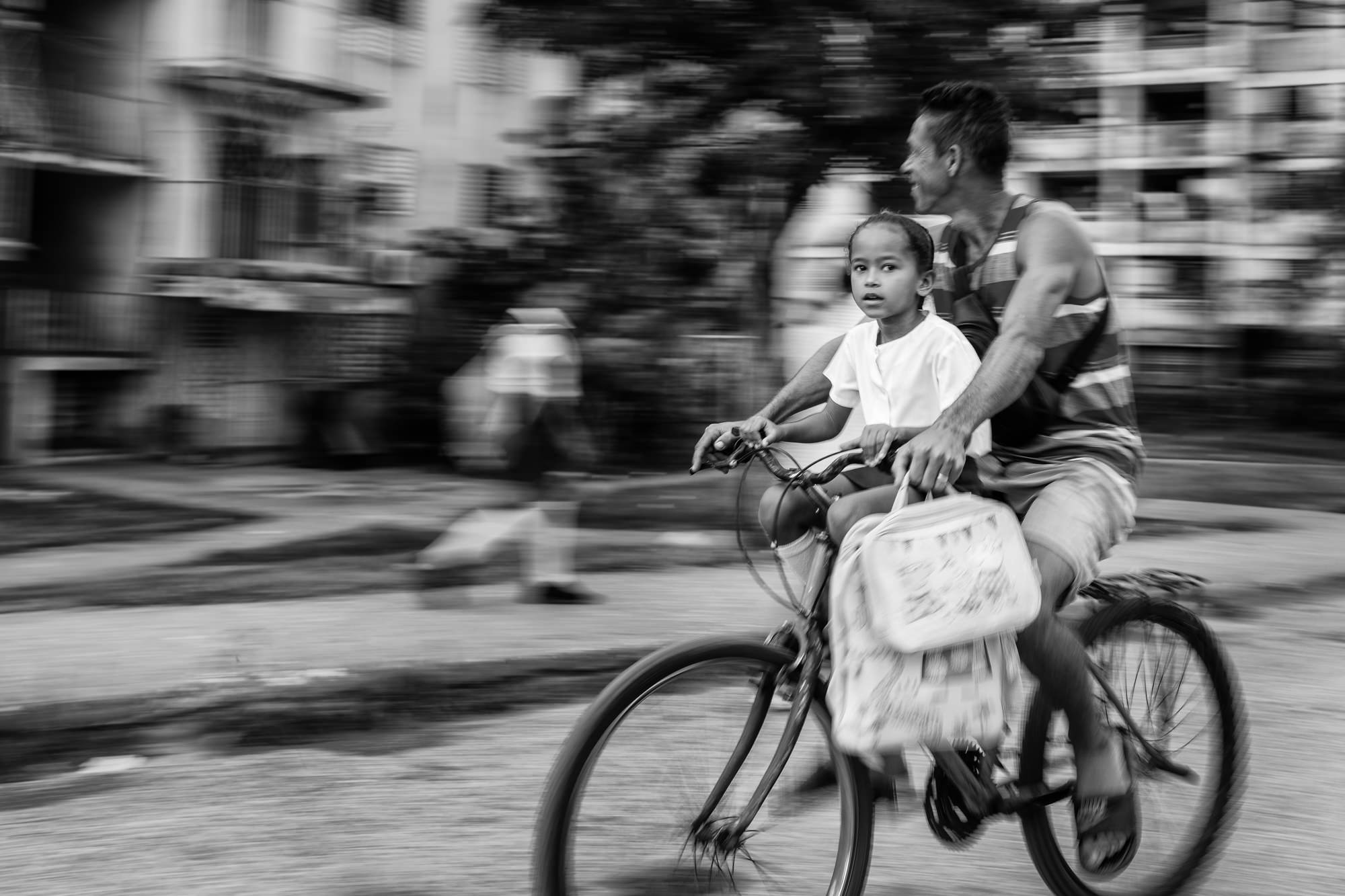 Cuba Street Photography Roadtrp | 14 Day Guide with Mark Seymour 21 “Father riding a bicycle with his child in front, captured in black and white with the background blurred in motion.”