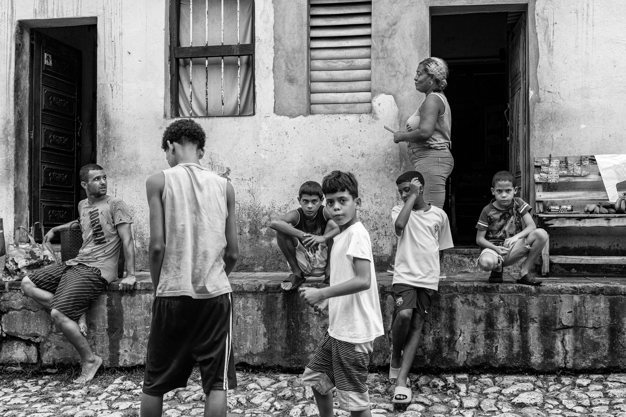 Cuba Street Photography Roadtrp | 14 Day Guide with Mark Seymour 19 “Black-and-white photo of boys playing and adults watching near the entrance of a weathered home with peeling walls.”