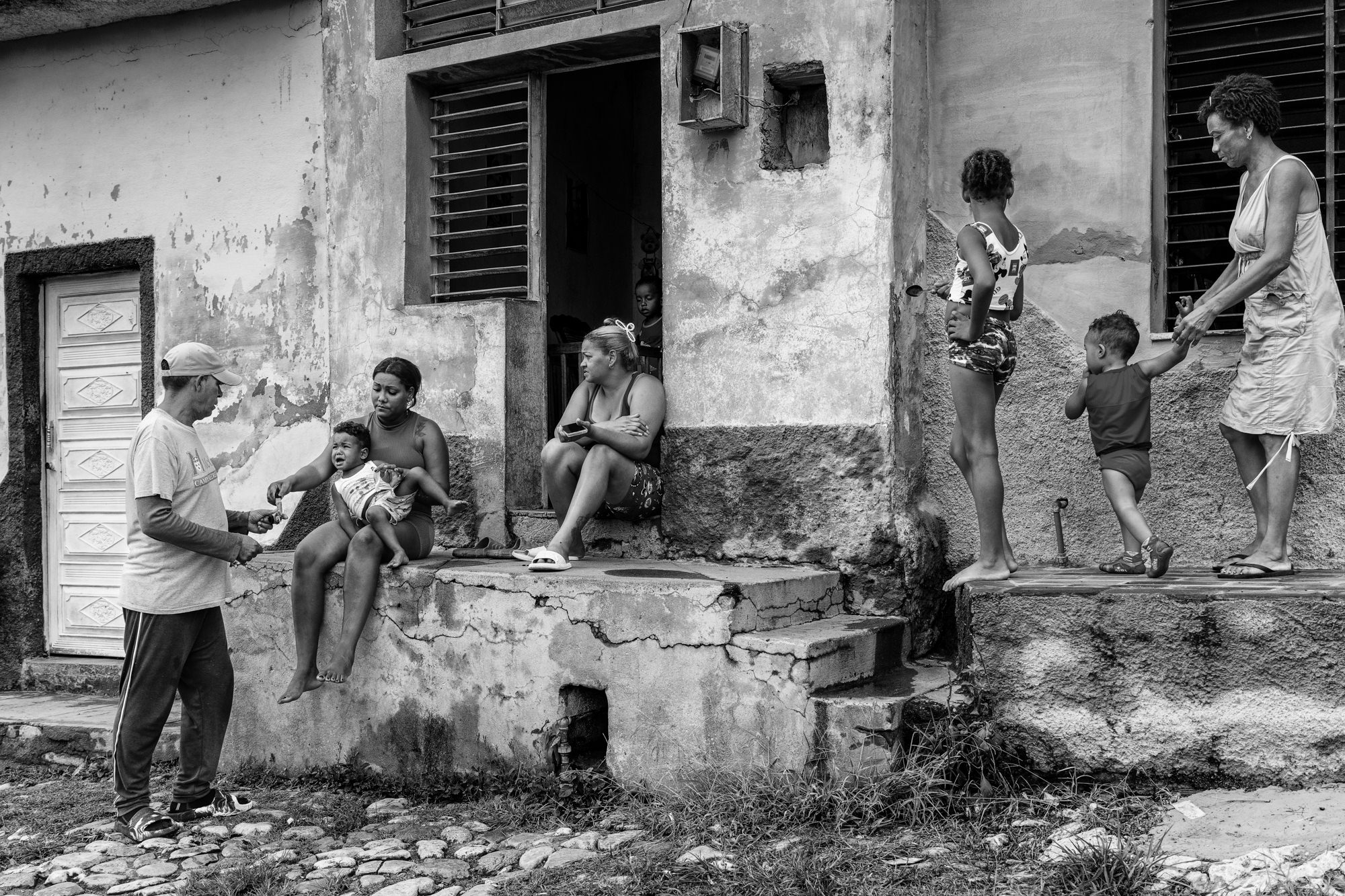 Cuba Street Photography Roadtrp | 14 Day Guide with Mark Seymour 18 A family gathered outside a weathered Cuban house, with a mother holding a crying baby while others sit and talk on the crumbling doorstep.