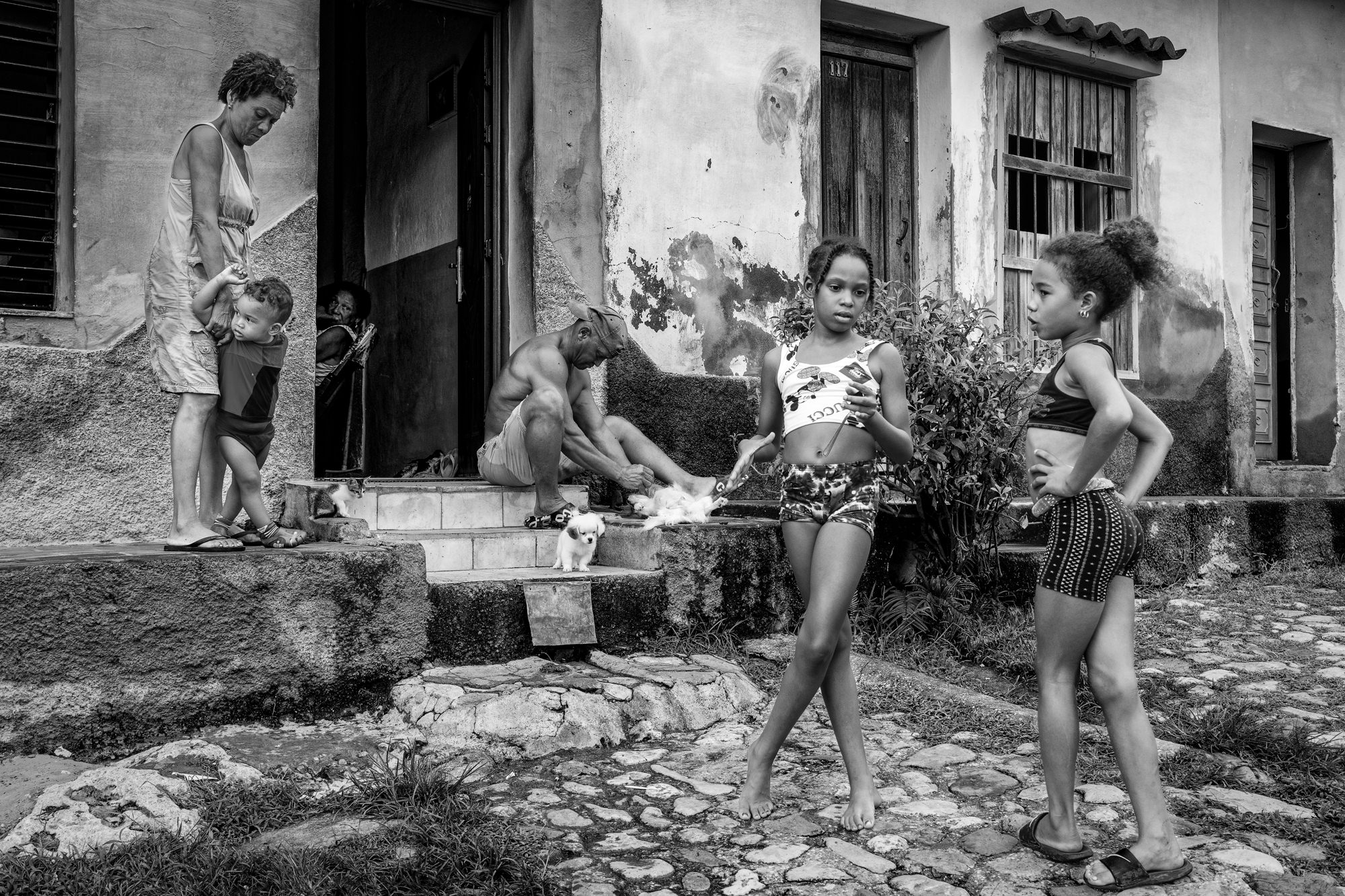 Cuba Street Photography Roadtrp | 14 Day Guide with Mark Seymour 17 Children, adults, and playful puppies gathered outside a rustic Cuban home, capturing a lively everyday moment on the doorstep.