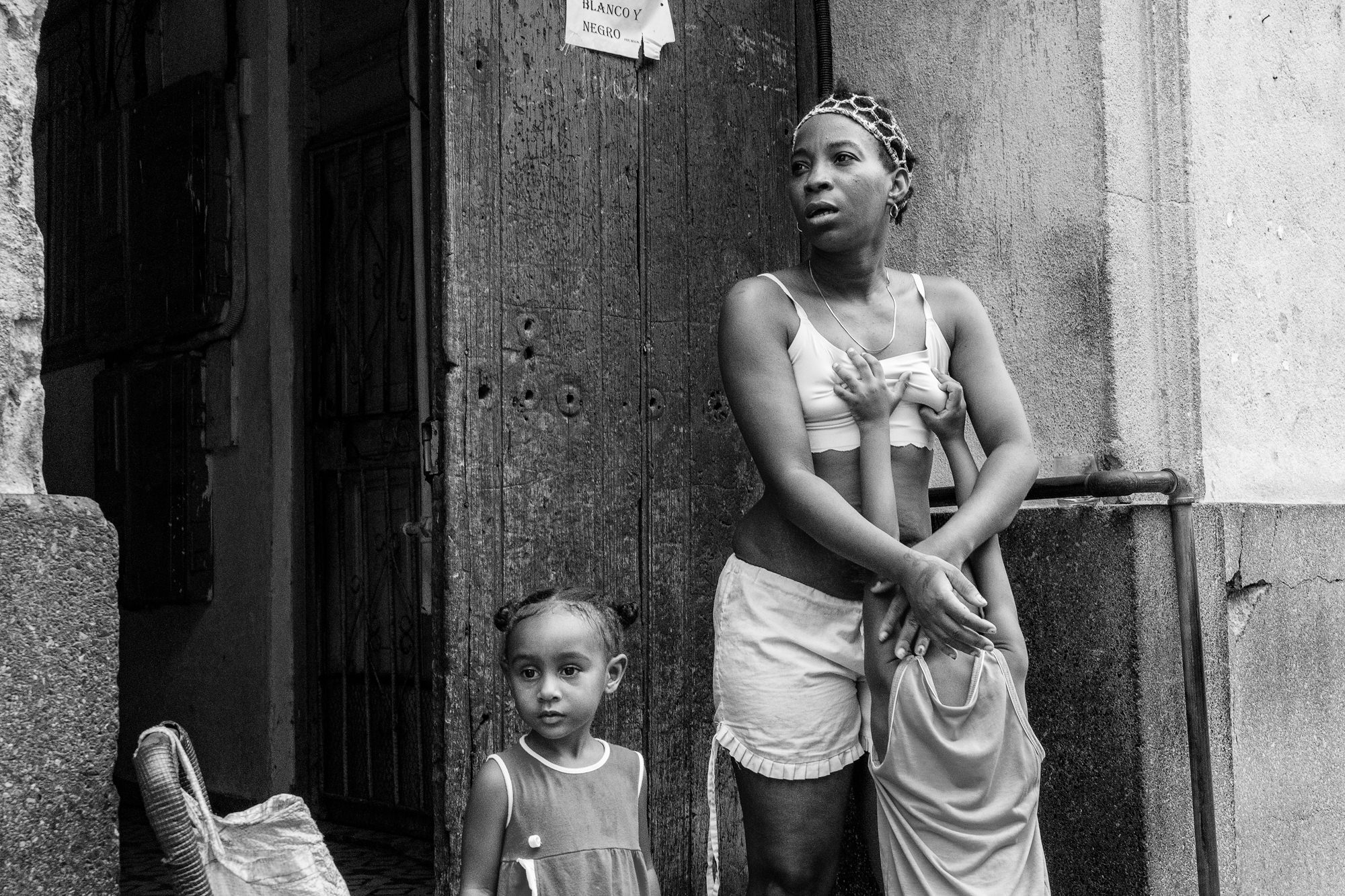 Cuba Street Photography Roadtrp | 14 Day Guide with Mark Seymour 16 A mother standing in a Cuban doorway with her two young daughters, one clinging to her as they look out onto the street.