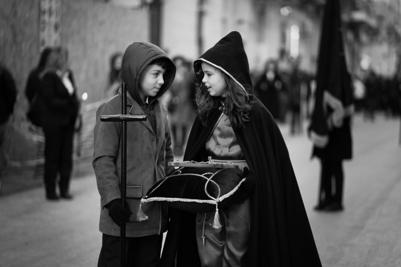 Inside the Misteri di Trapani: Documenting Sicily’s Living Tradition 24 Two children dressed in traditional procession clothing talk together while carrying ceremonial items during the Misteri di Trapani procession.