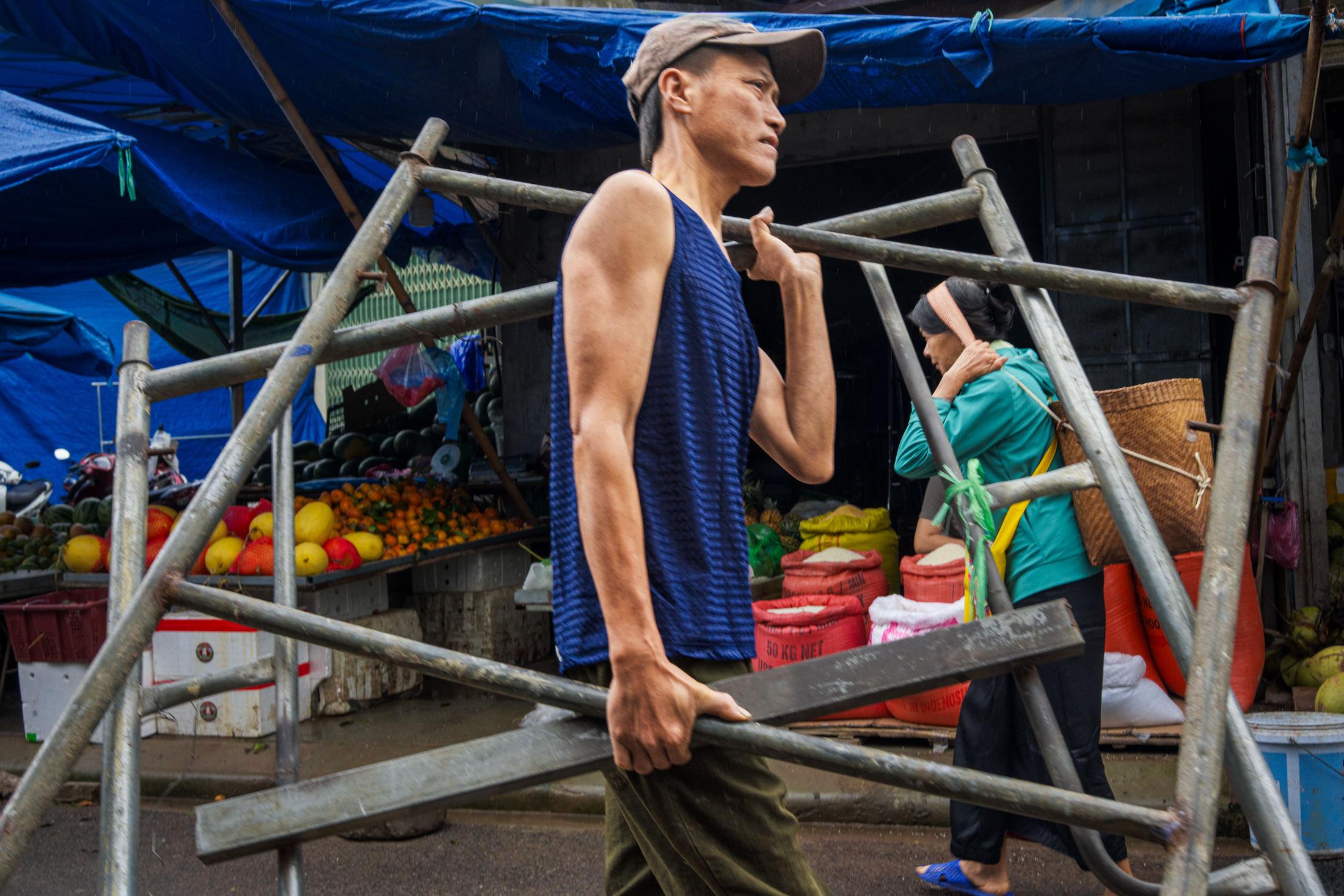 Northern Vietnam Photography: A Photographer’s Journey Beyond the Tourist Trail 24 A market worker carries a metal stall frame through a street market in Hanoi, Vietnam, during wet weather.