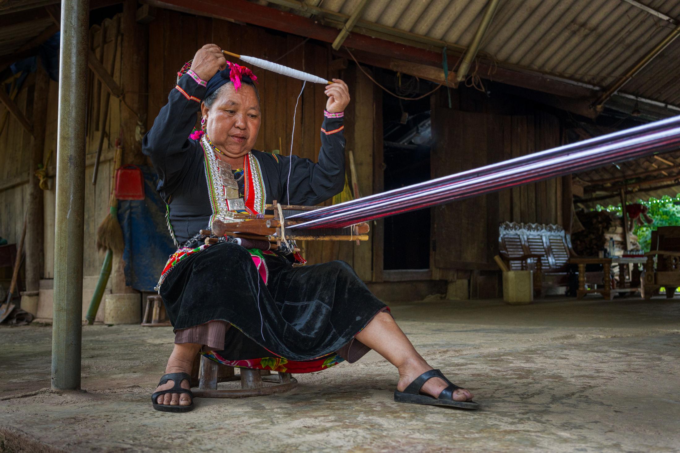 Northern Vietnam Photography: A Photographer’s Journey Beyond the Tourist Trail 19 A woman in traditional ethnic dress operates a backstrap loom outside her wooden home in northern Vietnam, weaving colourful fabric by hand.